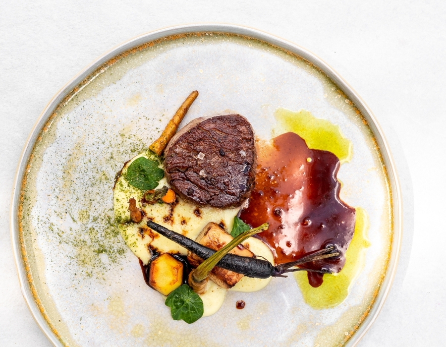 Jemný steak s omáčkou, bramborovou kaší, černou mrkví a ozdobnými bylinkami na stylovém talíři