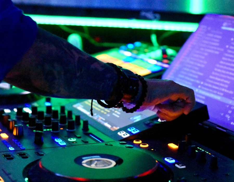 Ruka DJ ovládá mixážní pult s osvětlenými tlačítky a obrazovkami na hotelové párty