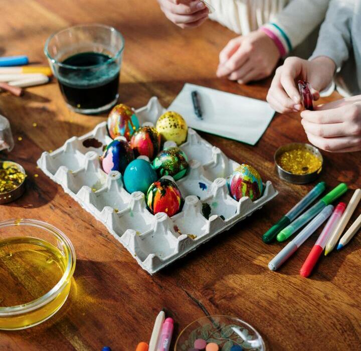 Kinder bemalen bunte Ostereier auf einem Holztisch mit Farben und Markern, eine festliche Atmosphäre.
