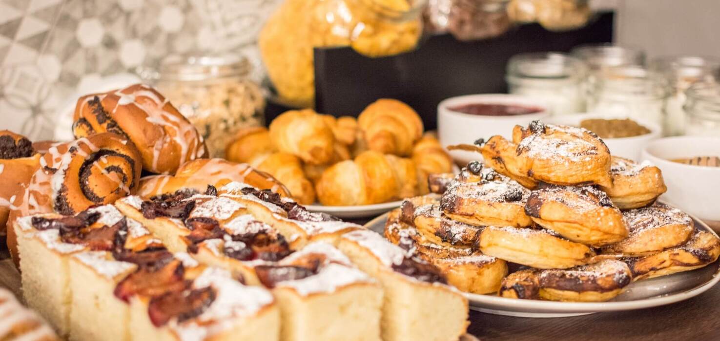 Bufet śniadaniowy z croissantami, słodkimi drożdżówkami, kawałkami ciasta z owocami i słoikami z musli