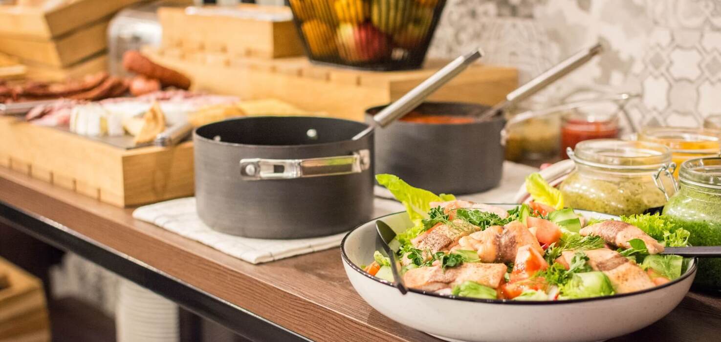 Stół bufetowy z sałatką z grillowanym łososiem, garnkami z sosami, chlebem i koszem świeżych owoców