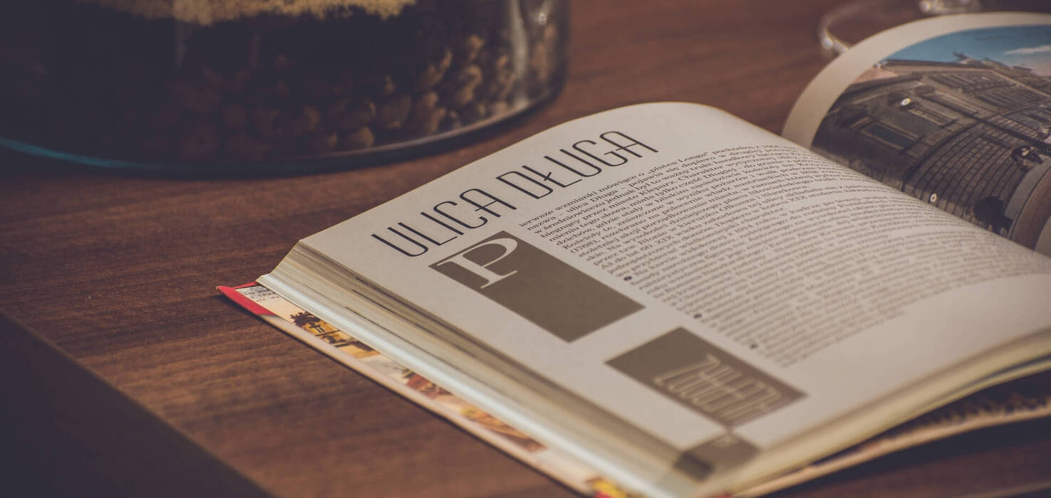Otwarty magazyn na drewnianym stoliku obok szklanego słoja z ziarnami i kieliszka, przytulny kącik do czytania.