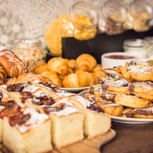 Bufet śniadaniowy z croissantami, słodkimi drożdżówkami, kawałkami ciasta z owocami i słoikami z musli