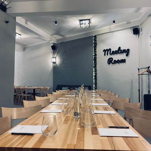 Sala spotkań z długim drewnianym stołem, szklankami i notatnikami, miękkie oświetlenie i napis 'Meeting Room'.