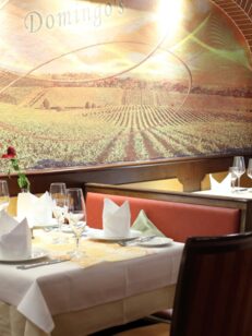 Eleganter Restaurantbereich mit weißen Tischdecken, gefalteten Servietten, Weingläsern und Wandmalerei eines Weinbergs