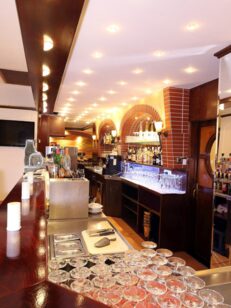 Gemütliche Hotelbar mit poliertem Holztresen, roten Polsterstühlen, Backsteinbögen mit Spirituosen und stimmungsvoller Beleuchtung