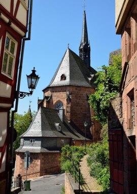 Historic stone church with steep slate roof and tall spire beside a cobblestone path and lush greenery