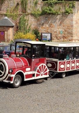 Red and white city train with passengers offering guided tours along a cobblestone street near historic stone walls