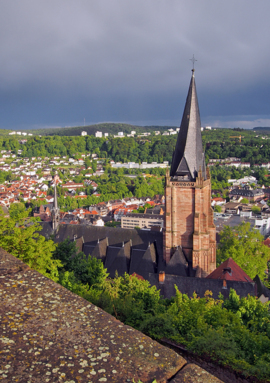 Historic church with tall spire overlooks lush green hills and town rooftops under moody sky