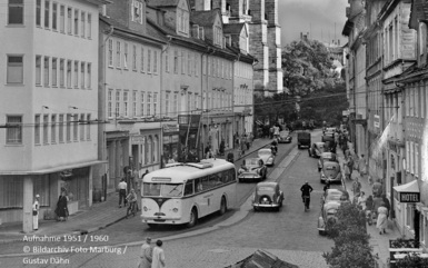 Historische europäische Straße mit Oldtimerautos, einem klassischen Bus, Fußgängern und einem Hotelschild an Kopfsteinpflaster