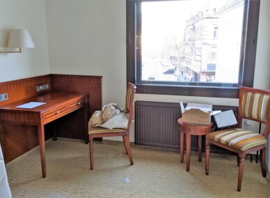 Gemütliche Hotelecke mit hölzernem Schreibtisch, zwei gestreiften Stühlen und Stadtblick durch großes Fenster