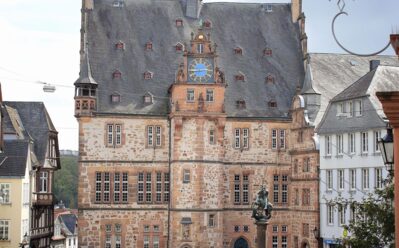 Historischer Marktplatz mit steinigem Gebäude und Uhrturm, Außen-Café und Besuchern, die die lebendige Atmosphäre genießen