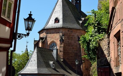 Historische Steinkirche mit steilem Schieferdach und hohem Turm neben Kopfsteinpflasterweg und grünem Bewuchs