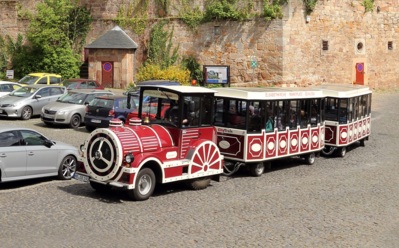 Roter und weißer Stadtexpress mit Fahrgästen auf Kopfsteinpflasterstraße neben historischen Steinmauern