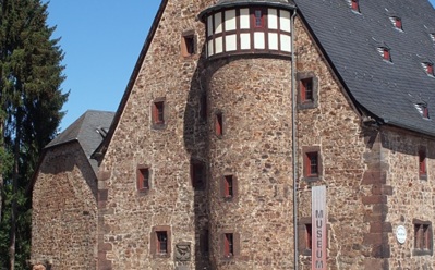 Historisches Steingebäude mit steilem Schieferdach und kleinen Fenstern, beherbergt Museum an ruhiger Straße bei klarem Himmel