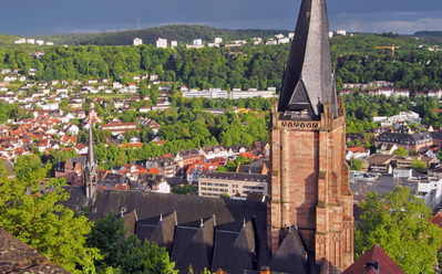 Historische Kirche mit hohem Turm überblickt grüne Hügel und Stadt unter bewölktem Himmel