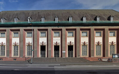 Historisches Museumsgebäude mit symmetrischen Fenstern und dekorativen Eisenarbeiten an einer Stadtstraße unter blauem Himmel