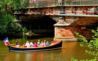 Gruppe von Touristen auf einer Bootstour unter einer historischen Steinbrücke, umgeben von grünen Bäumen