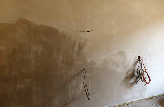 Unfinished hotel room wall with exposed electrical wiring and rough plaster, showing ongoing renovation work.