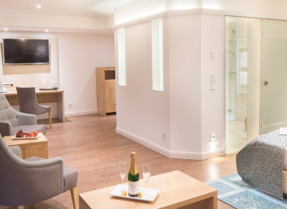 Helle Hotelsuite mit Sitzbereich, Holzboden, modernen Möbeln, Kingsize-Bett mit gemustertem Bezug und Champagner auf dem Couchtisch