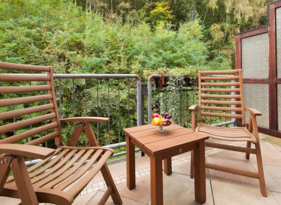 Gemütlicher Balkon mit zwei Holzstühlen und Tisch mit Obstschale, umgeben von üppigem Grün für eine ruhige Auszeit