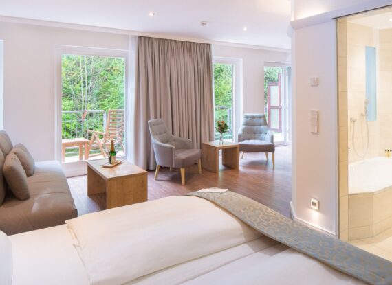 Helle Hotel-Suite mit Kingsize-Bett, gemütlicher Sitzecke, Balkon mit Blick ins Grün und modernem Bad mit Wanne und Dusche