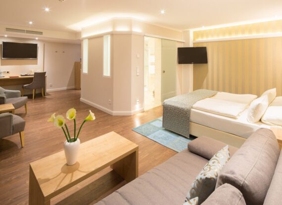 Geräumige Hotelsuite mit Kingsize-Bett, gemütlicher Sitzecke, Holzboden, Schreibtisch, Flachbildfernsehern und sanfter Umgebungsbeleuchtung