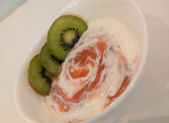 Schale mit cremigem Joghurt, vermischt mit Fruchtpüree, dazu frische Kiwischeiben als Beilage
