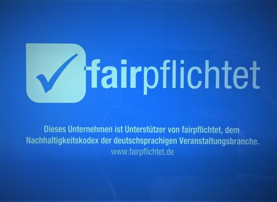 Blauer Hintergrund mit fairpflichtet-Logo und Häkchen, Text zur Unterstützung des Nachhaltigkeitskodex der deutschsprachigen Veranstaltungsbranche