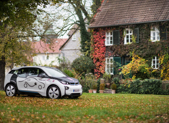 Elektroauto auf einer Wiese vor einem reizvollen Gästehaus mit efeubewachsenen Wänden und bunter Herbstlaubkulisse