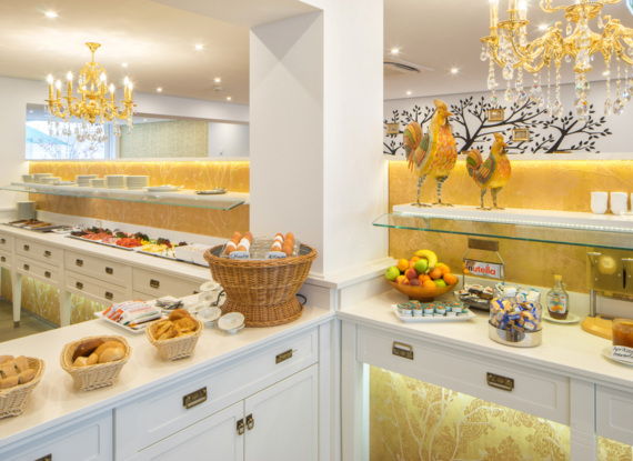Helles Frühstücksbuffet im Hotel mit frischem Brot, gekochten Eiern, Obstschale, kalten Aufschnitt, goldenen Kronleuchtern und Dekohähnen
