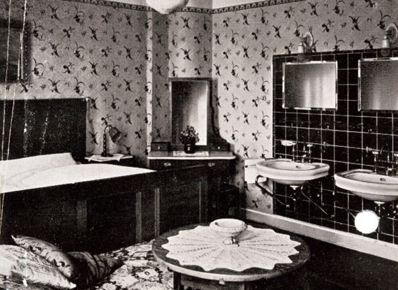 Hotelzimmer im Vintage-Stil mit floraler Tapete, Doppelwaschbecken, Holzbett, Schminktisch mit Spiegel und rundem Tisch mit Spitzenüberzug