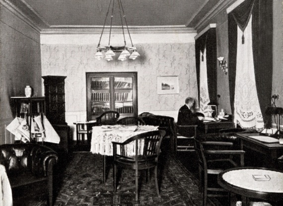 Elegante Vintage-Hotel-Lounge mit Holzstühlen, Ledersofa, gemusterten Vorhängen und einem Gast, der am Fenster liest