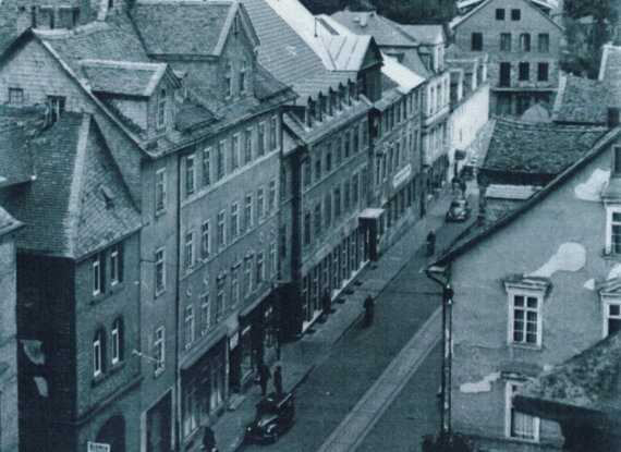 Historische europäische Straßenszene mit alten Steingebäuden, steilen Dächern und schmalen Gehwegen an einer ruhigen Straße.