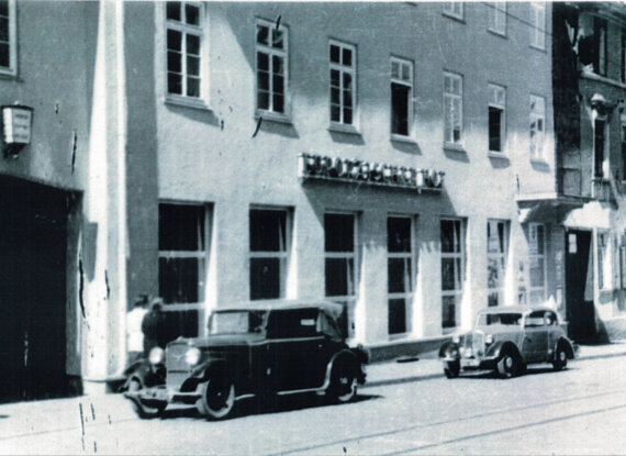 Historische Hotelfassade mit alten Autos, die an einer ruhigen Straße unter großen mehrteiligen Fenstern geparkt sind