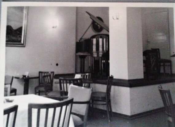 Klassische Hotellounge mit Holzstühlen, weiß gedeckten Tischen und einem Flügel in einer gemütlichen Ecke.