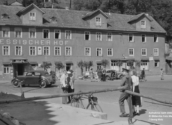 Historisches Hotel Hessischer Hof mit klassischen Autos und Gästen in zeittypischer Kleidung auf ruhigem Stadtplatz