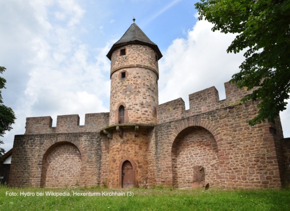 Historische Steinmauer mit gewölbten Nischen und rundem Turm mit spitzem Dach, umgeben von Grünanlagen