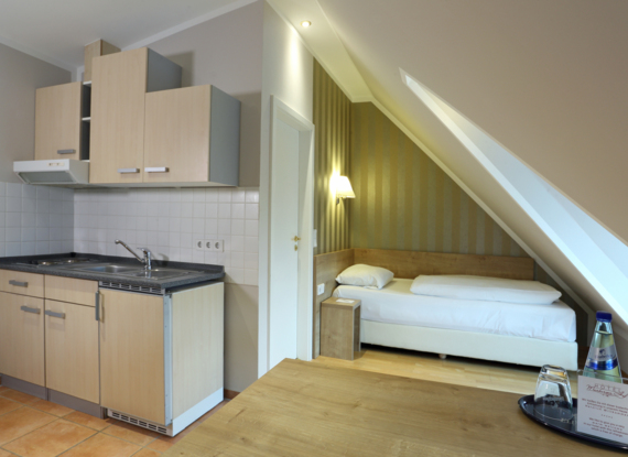 Gemütliches Hotelzimmer im Dachgeschoss mit Einzelbett, kleiner Küchenzeile, schrägem Dachfenster und kostenlosem Wasser auf Holztisch