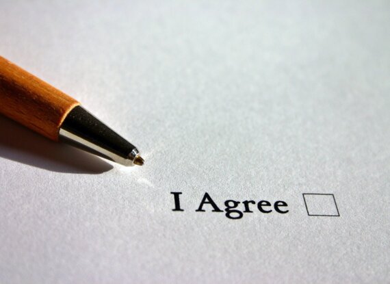 Nahaufnahme einer Kugelschreiberspitze neben einem leeren Kontrollkästchen mit der Aufschrift 'Ich stimme zu' auf weißem Papier