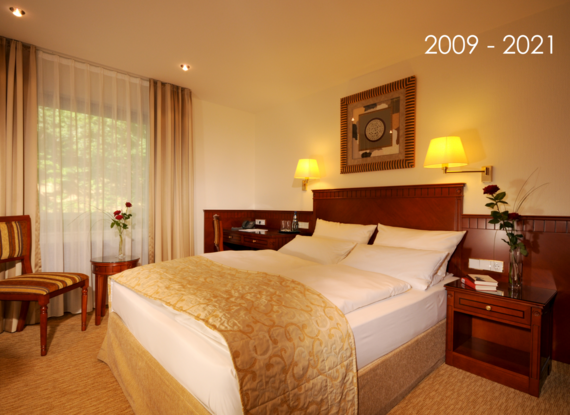 Classic hotel room with queen bed, warm lighting, wooden furniture, elegant decor, and fresh roses on side tables near window with curtains