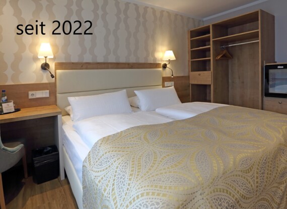 Cozy hotel room featuring twin beds with patterned bedspread, wooden furniture, desk, minibar, and warm bedside lighting