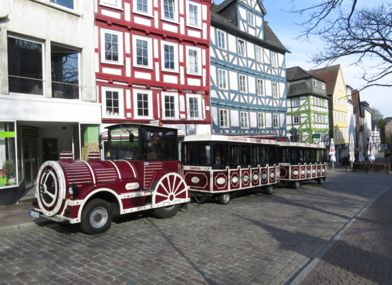 Touristenstadtbahn auf Kopfsteinpflaster vor bunten, historischen Fachwerkhäusern geparkt