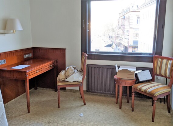Cozy hotel corner with wooden writing desk, two striped chairs, and a city view through a large window