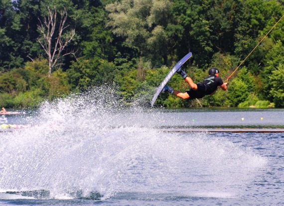 Gast beim Wakeboarden auf einem See, umgeben von dichtem Grün, genießt aktiven Wassersport an sonnigem Tag
