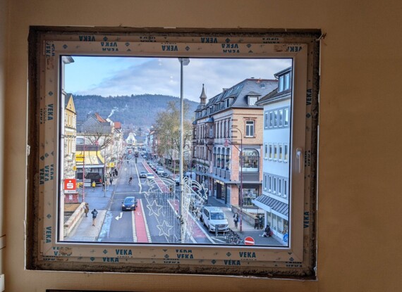 View through a large window showing a lively street with historic buildings, pedestrians, and holiday light decorations