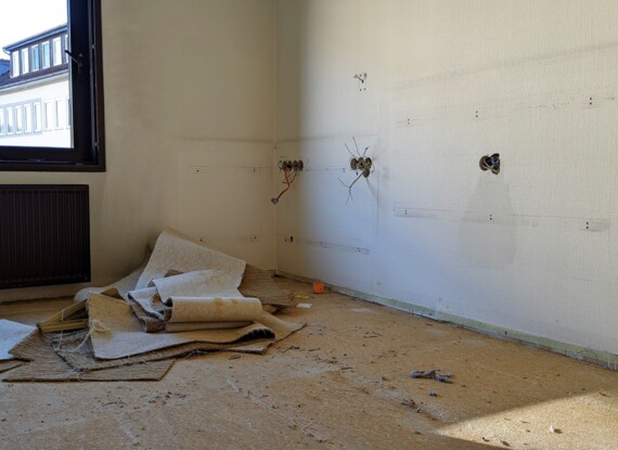 Vacant hotel room under renovation with exposed wiring in walls and old carpet removed, natural light from open window