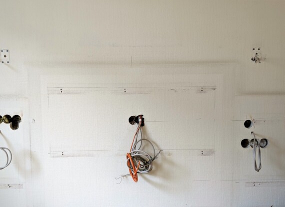 Plain wall with exposed wiring and mounting holes, likely part of ongoing hotel room renovation or repair work