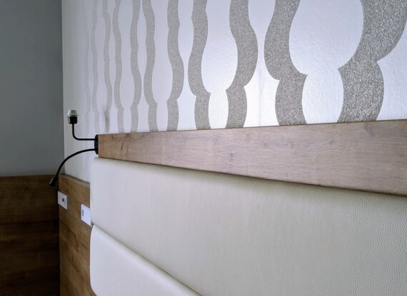 Close-up of a hotel room headboard with padded cream leather, natural wood trim, and modern patterned wallpaper