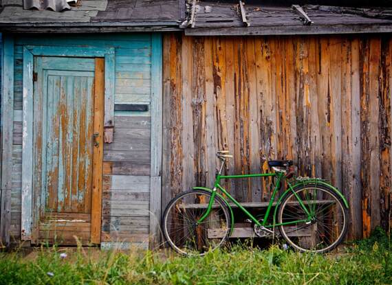 Rustikale, verwitterte Holzhütte mit türkisfarbenem Türrahmen und einem vintage grünen Fahrrad davor geparkt